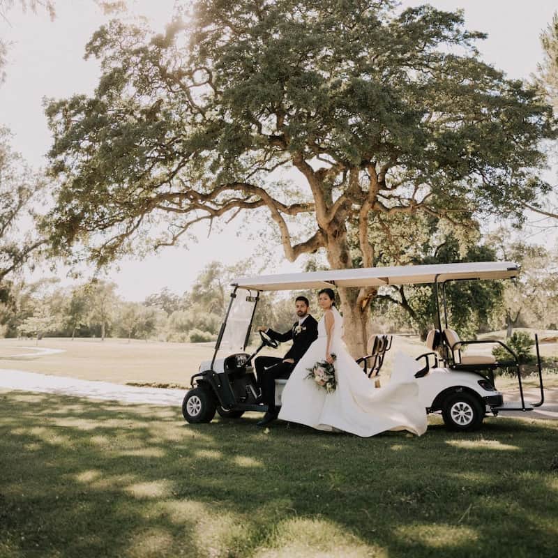 Bride and groom beside a golf cart beneath a large oak tree at a scenic Sacramento golf course wedding venue.