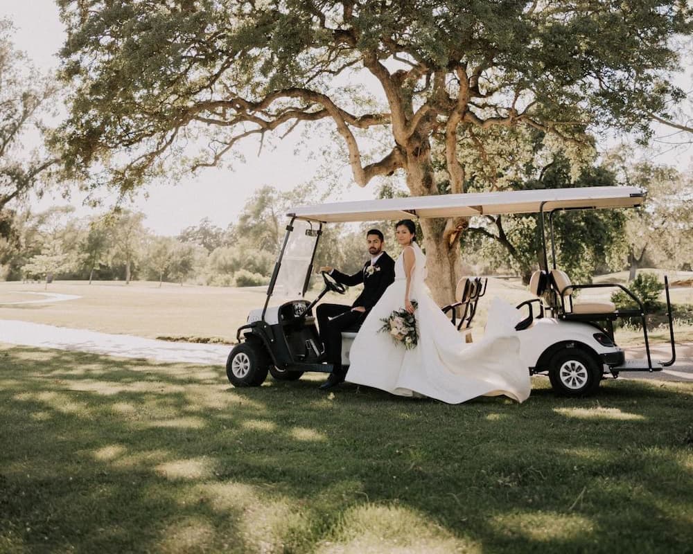 Bride and groom beside a golf cart beneath a large oak tree at a scenic Sacramento golf course wedding venue.