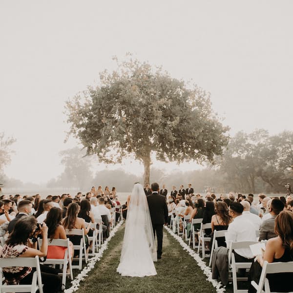 Outdoor wedding ceremony at the Pavilion at Haggin Oaks with the bride and groom walking down the aisle surrounded by guests.